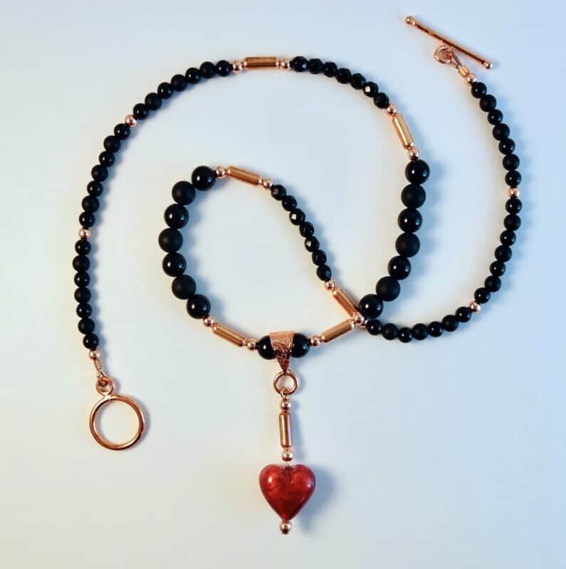 Black beaded necklace with gold accents, featuring a small red heart pendant in the center.