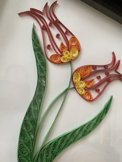 Quilled paper art depicting two tulip flowers with green leaves and stems on a white background.