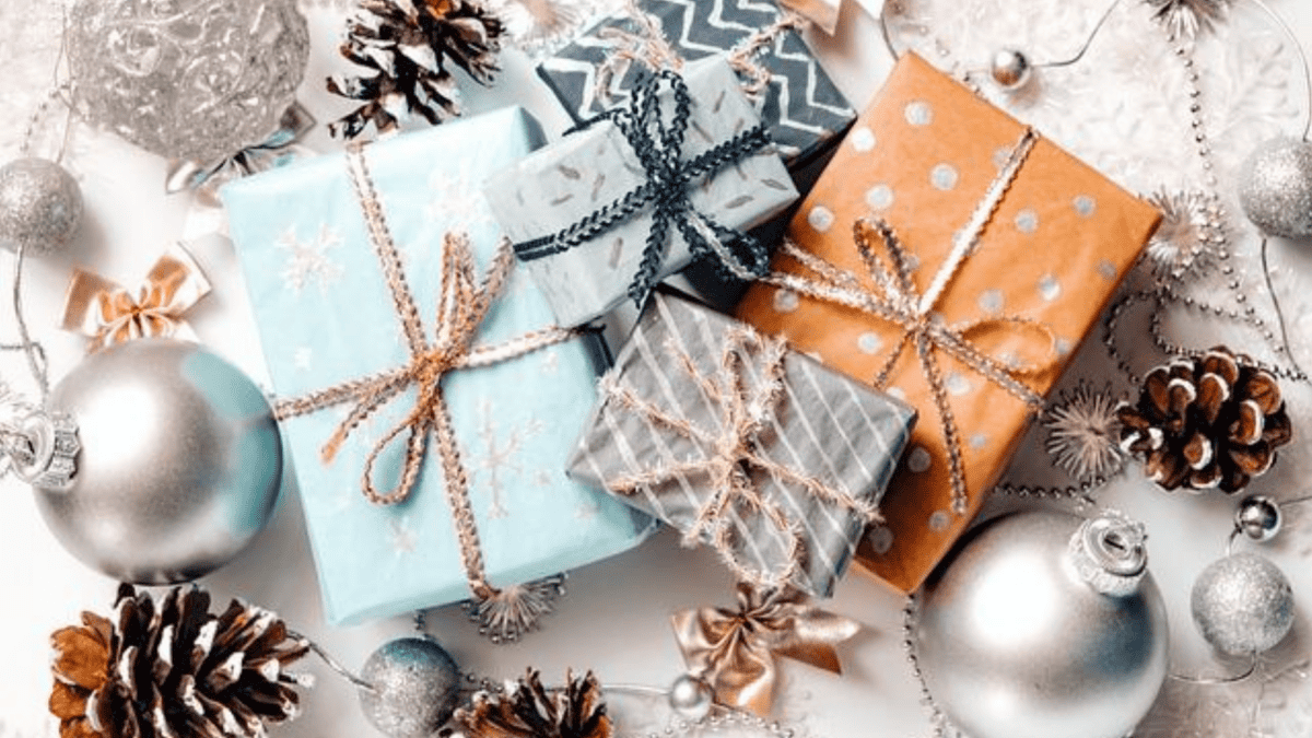 Wrapped gifts with decorative ribbons surrounded by silver baubles, pinecones, and festive holiday ornaments.