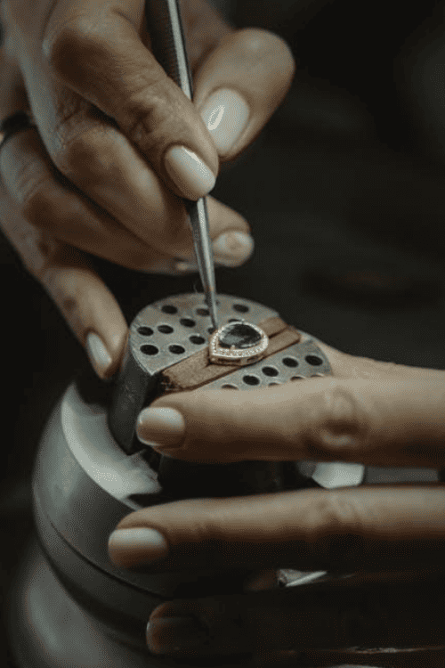 Close-up of a jeweler's hands working on a gemstone ring with a tool.