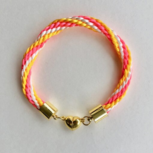 Colorful braided bracelet with yellow, pink, and white strands, featuring a gold clasp and a heart-shaped charm in the middle.