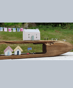 Miniature wooden houses with drying clothes and small flags, set in a carved wooden structure, against a green garden backdrop.