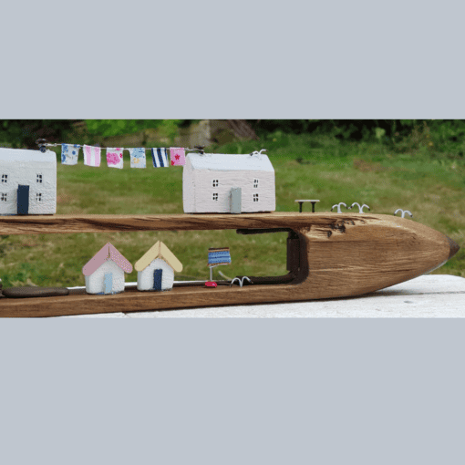 Miniature wooden houses with drying clothes and small flags, set in a carved wooden structure, against a green garden backdrop.