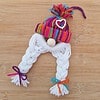 Handmade yarn gnome with a rainbow hat, white braided beard, and colorful bows, on a wooden surface.