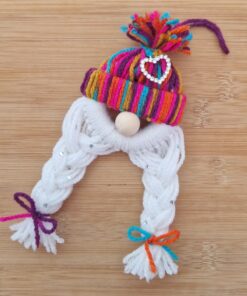 Handmade yarn gnome with a rainbow hat, white braided beard, and colorful bows, on a wooden surface.