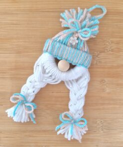 Handmade yarn ornament resembling a winter hat with braided tassels tied with bows on a wooden surface.