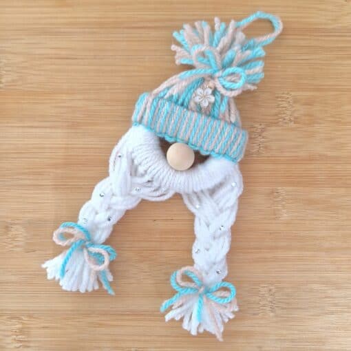 Handmade yarn ornament resembling a winter hat with braided tassels tied with bows on a wooden surface.