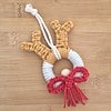 Macrame reindeer ornament with brown antlers, white face, red nose, and red bow against a wooden background.