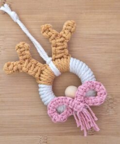 Handmade crochet reindeer ornament with brown antlers, white ring body, pink bow, and a hanging loop on a wooden surface.