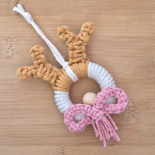 Handmade crochet reindeer ornament with brown antlers, white ring body, pink bow, and a hanging loop on a wooden surface.