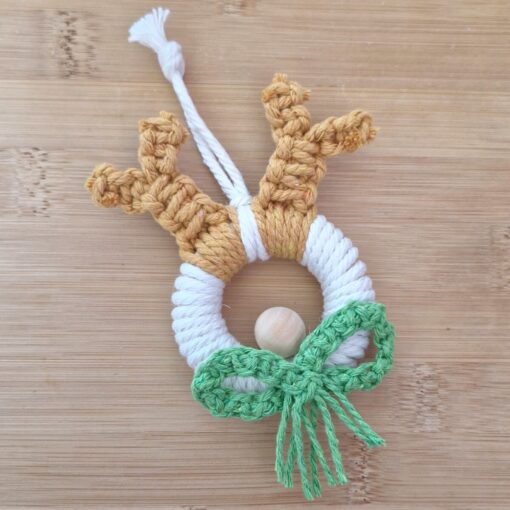 Handmade decoration with a wooden ring wrapped in white string, adorned with brown antlers and a green crocheted bow.