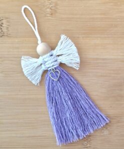 Handmade purple tassel with white wings, wooden bead head, and heart charm on wooden background.