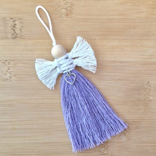 Handmade purple tassel with white wings, wooden bead head, and heart charm on wooden background.