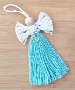 Handmade yarn angel ornament with white wings, turquoise tassel dress, wooden bead head, and heart charm, on a wooden background.