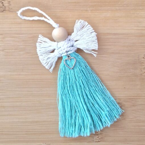 Handmade yarn angel ornament with white wings, turquoise tassel dress, wooden bead head, and heart charm, on a wooden background.