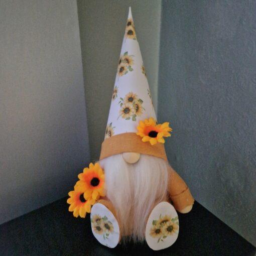 Gnome with a white beard wearing a tall hat, yellow outfit, and sunflowers as decorations, sitting on a dark surface.