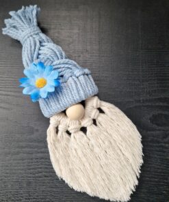 Macrame gnome with a blue hat, decorated with a blue flower, and a long white beard, on a dark wooden surface.