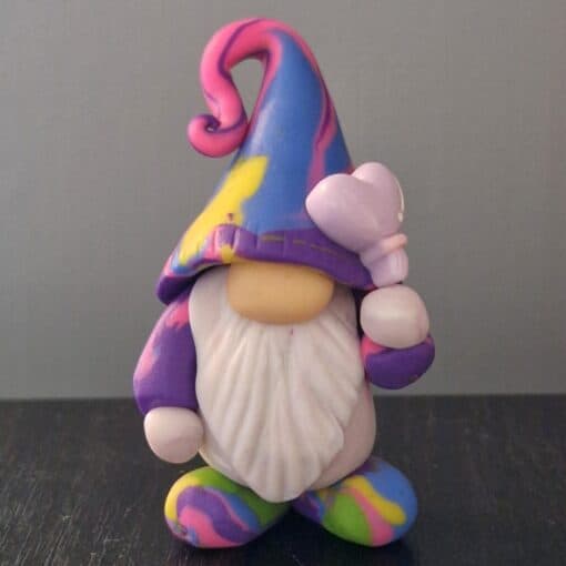 Colorful gnome figurine with a rainbow-patterned hat and beard, holding a butterfly on a dark surface.