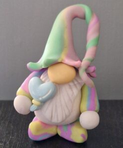 A small gnome figurine with a pastel-colored outfit and hat, holding a blue heart-shaped object, standing on a dark surface.