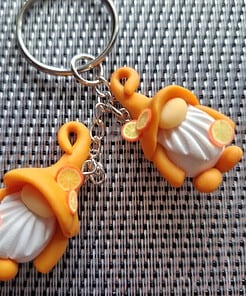 Keychain with two orange-hatted festive gnome figurines on a woven gray and white background.