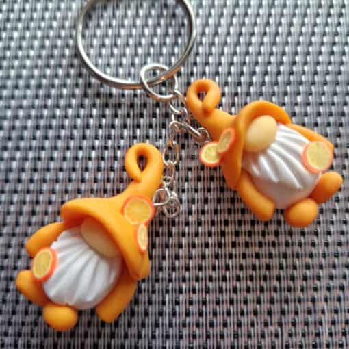 Keychain with two orange-hatted festive gnome figurines on a woven gray and white background.