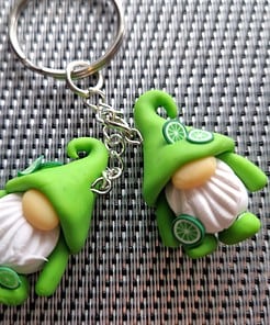 Keychain with two green hat gnome charms on a textured black and white background, featuring small lime slice decorations.