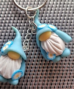 Two blue, flower-decorated gnome keychains with white beards and yellow noses on a silver key ring on a textured background.