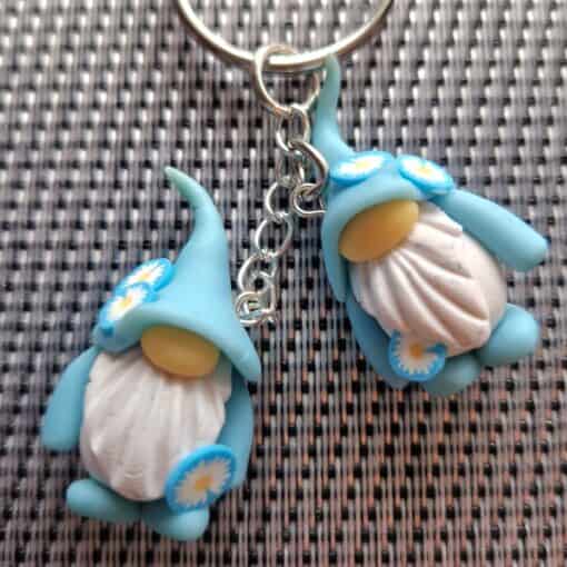 Two blue, flower-decorated gnome keychains with white beards and yellow noses on a silver key ring on a textured background.