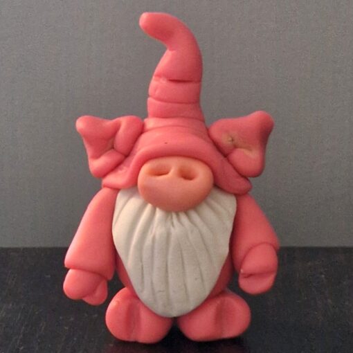 Pink clay gnome with a tall hat, large nose, and white beard, standing against a gray background.