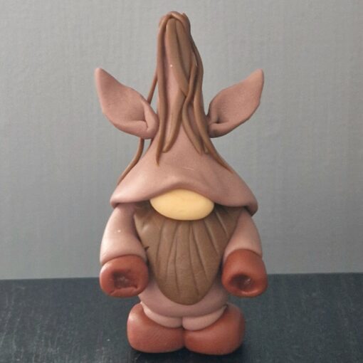 Clay figurine resembling a gnome with a tall hat, large ears, brown outfit, and beard on a black surface against a gray background.