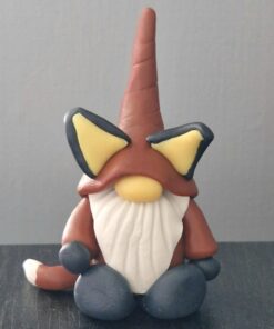 Small gnome figurine with a tall hat, white beard, and oversized ears, sitting on a dark surface against a plain background.