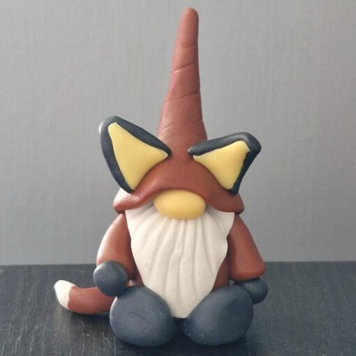 Small gnome figurine with a tall hat, white beard, and oversized ears, sitting on a dark surface against a plain background.