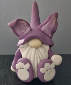 Clay figurine of a gnome with a purple hat, large ears, a white beard, and purple shoes with white detailing.