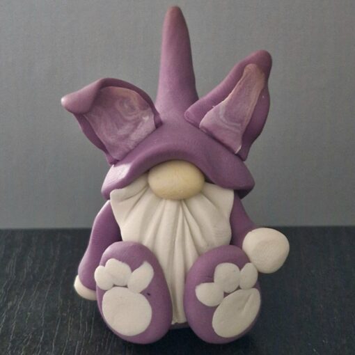 Clay figurine of a gnome with a purple hat, large ears, a white beard, and purple shoes with white detailing.