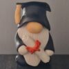 Clay gnome figurine wearing a graduation cap and holding a diploma tied with a red ribbon.