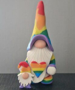 Two gnome figurines in rainbow attire holding a heart with the same colors, set against a plain background.