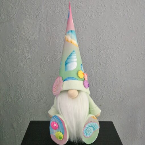 A gnome figurine with a long white beard, wearing a pastel sea-themed hat and matching shoes, sits against a textured wall.