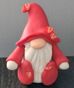 Small gnome figurine with a red hat, white beard, and red outfit, sitting on a dark surface against a gray background.