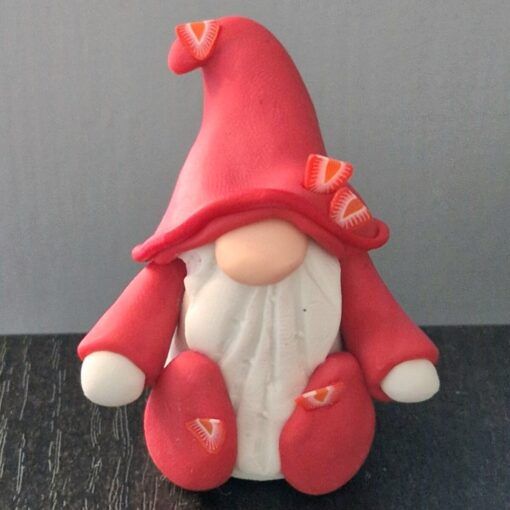 Small gnome figurine with a red hat, white beard, and red outfit, sitting on a dark surface against a gray background.