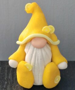 A gnome figurine wearing a yellow hat adorned with lemon slices, a white beard, and yellow attire sits against a dark surface.