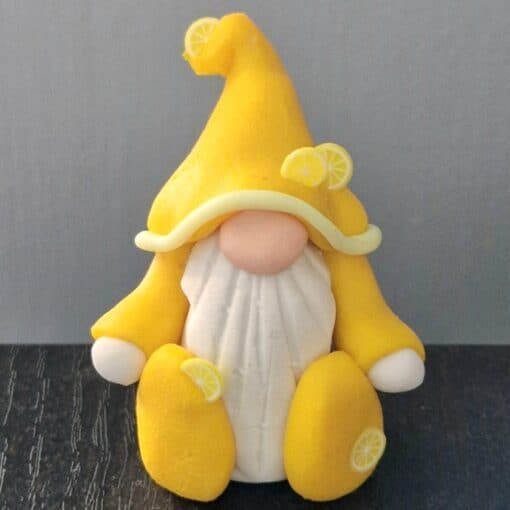 A gnome figurine wearing a yellow hat adorned with lemon slices, a white beard, and yellow attire sits against a dark surface.