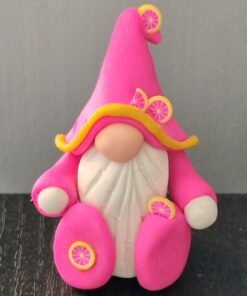 Clay gnome figure with a pink hat and robe, adorned with lemon slices, sitting on a dark surface.