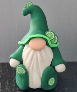 Clay figurine of a gnome with a white beard, wearing a green hat and coat decorated with lime slices, on a dark surface.