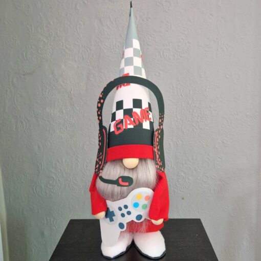 A gnome figurine dressed as a gamer, wearing a cone hat with "GAME" text, headphones, and holding a game controller.