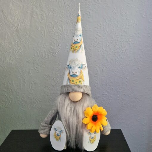 Gnome figurine with white hat and boots featuring cow prints, holding a yellow flower, sits against a textured gray background.