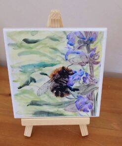 A watercolor painting of a bumblebee on a purple flower, displayed on a small wooden easel against a light background.