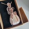 A copper wire-wrapped teardrop pendant with an intricate design, displayed in a black velvet box.