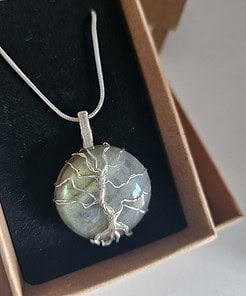 Silver pendant with a wire-wrapped tree design, set in a round labradorite stone, displayed in an open cardboard box.