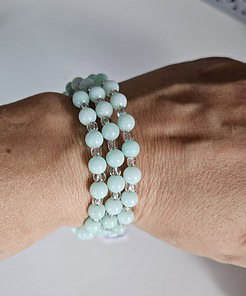 Close-up of a wrist wearing three strands of round light blue beads with clear spacers on a bracelet.