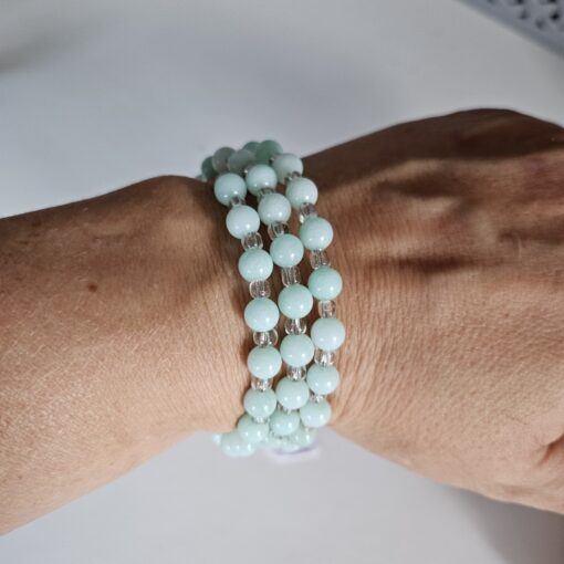 Close-up of a wrist wearing three strands of round light blue beads with clear spacers on a bracelet.